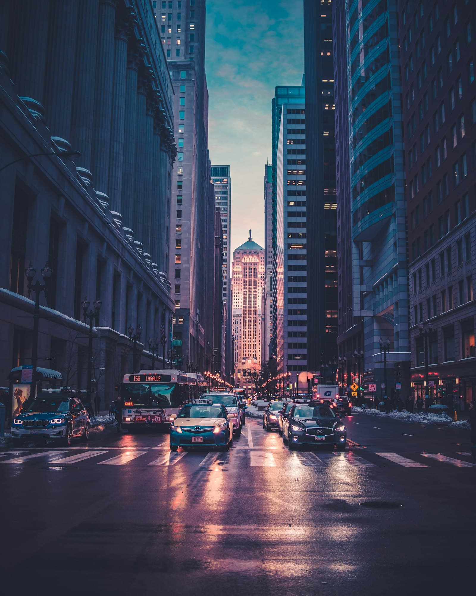 City street canyon between illuminated mixed-use buildings at dusk